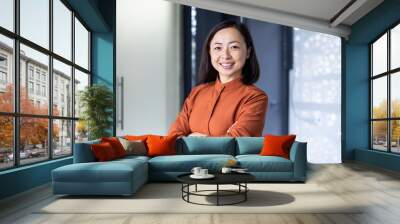 Portrait of young beautiful and successful Asian business woman, female employee smiling and looking at camera with crossed arms, financial woman satisfied with the results of her work achievement. Wall mural