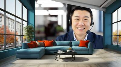 Professional Asian male in a blue suit with a headset smiling confidently in a corporate office setup, representing customer support. Wall mural