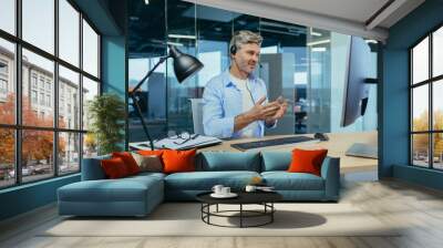 Senior and experienced employee, advises the buyer on a video call, the man works in a modern office uses a headset for negotiations, and a webcam Wall mural