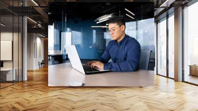 Serious and thoughtful businessman working inside office sitting at table using laptop at work, mature asian boss in shirt thinking and typing on keyboard. Wall mural