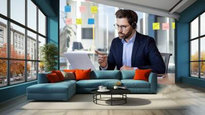 Serious confident man with headset phone and laptop using video call for remote communication, businessman investor at remote meeting explaining success plan to colleagues and partners. Wall mural