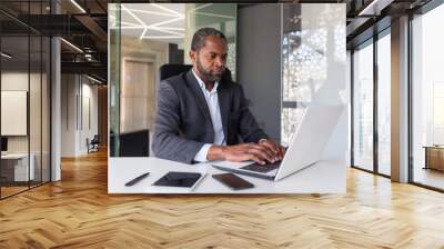 Serious mature businessman working on laptop inside office at workplace, african american boss thoughtful in business suit, successful experienced investor banker. Wall mural