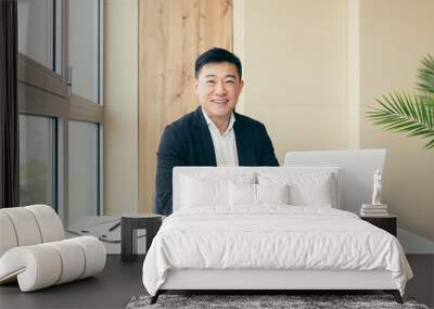 Successful Asian businessman, in a black business suit, works on a laptop, relaxes in a stylish office Wall mural