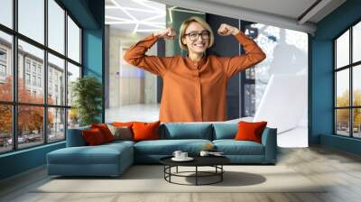 Successful strong and confident businesswoman smiling and looking at camera, female worker at workplace superhero inside office using laptop. Wall mural