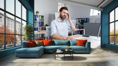 The man works in the office, the patient has a severe headache, upset businessman sitting at the table, holding his hands behind his head Wall mural