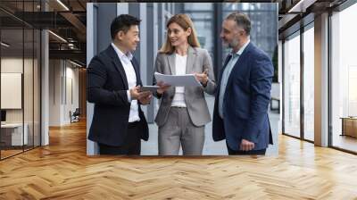 Three businessmen outside office building with documents discussing plans, businessmen and businesswoman having fun chatting and talking, diverse business group in business suits Wall mural