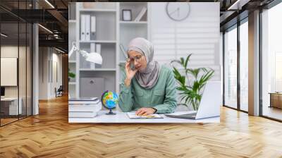 Tired and tired online teacher, woman in hijab working in home office remotely, teaching students and pupils, using laptop at work Wall mural