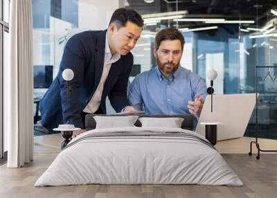 Two businessmen in suits work in the office, look at a laptop, discuss work issues, have a discussion. Wall mural