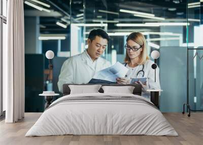 Two doctors, mixed race Asian man and Caucasian woman, communicate, discuss patient treatment, work in a modern clinic Wall mural