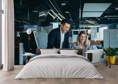 Two employees in a modern office, an Asian man and a woman working at a table, colleagues discussing and consulting, thinking about a joint project Wall mural