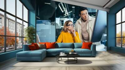 Two freelancers, an Asian man and a woman, work in a modern office, discussing and discussing a joint project, looking at a computer monitor Wall mural