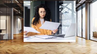 Upset and disappointed business woman reviews documents financial reports contracts, female employee is dissatisfied with the financial result income, seriously reads before thinking . Wall mural