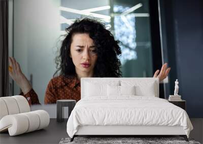 Upset and nervous business woman looking at laptop screen, female worker working inside office building, frustrated and dissatisfied with result, spreading hands. Wall mural