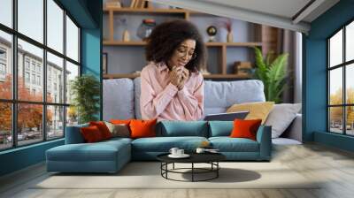 Woman crying during an online therapy session with psychologist. Emotional video call on laptop while sitting on a sofa in cozy living room at home. Mental health therapy and support. Wall mural