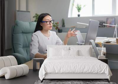 Young beautiful Asian female doctor consults patients remotely online consultation, woman works in office uses computer and web camera for video call. Wall mural