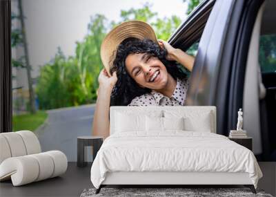 Young girl traveling by car, hispanic woman with curly hair looking out the window, enjoying vacation and travel. Wall mural