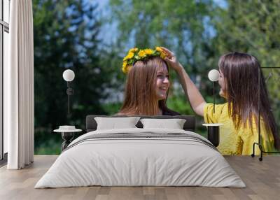 Young sisters in nature weave a wreath of dandelions. Talk and enjoy the rest. Weave flowers into the hair Wall mural