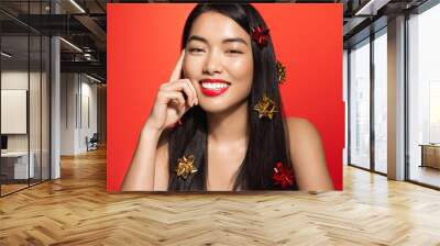 Beautiful asian woman with red lips, glowing clear skin, has smooth shiny hair with chrismas gift wrap, standing over studio background Wall mural