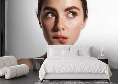 Beauty face and spa. Woman with freckles, clean nourished skin, biting lip and look aside. Girl model using antiaging cosmetics and vitamin c serum for bettet smoother skin tone, white background Wall mural