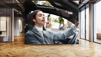 Businesswoman sitting in car and using lipstick, looking at herself in rear-view mirror to check on makeup Wall mural