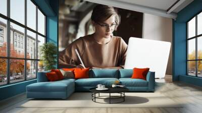 creative good-looking european female with fair hair in trendy glasses, making notes while looking a Wall mural