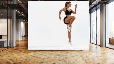 Determined muscular female athlete workout, raising leg and doing stretching exercises. Sport woman in sportswear training indoors, doing fitness aerobics, white background Wall mural