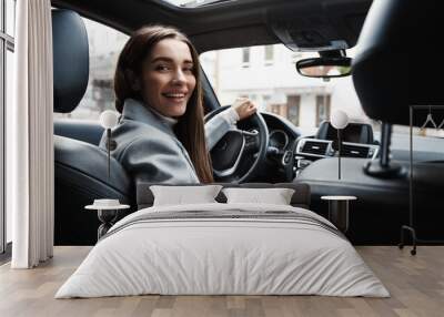 Elegant woman driver looking at backseat, smiling happy, asking passanger fasten seatbelt. Businesswoman talking to person in her car, driving at work Wall mural