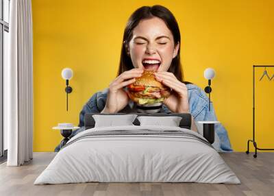 Girl bites cheeseburger with pleasure. Woman eating hambuger, order burger for takeaway food delivery at fastfood restaurant Wall mural