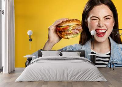 Happy smiling woman posing with cheeseburger, holding big tasty burger, enjoyment face, yellow background Wall mural