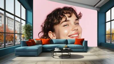 Skin care. Woman with beauty face and healthy facial skin portrait. Beautiful curly girl model with natural makeup touching glowing hydrated skin on pink background closeup. High quality image Wall mural