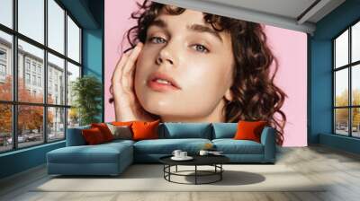 Skin care. Woman with beauty face and healthy facial skin portrait. Beautiful curly girl model with natural makeup touching glowing hydrated skin on pink background closeup. High quality image Wall mural