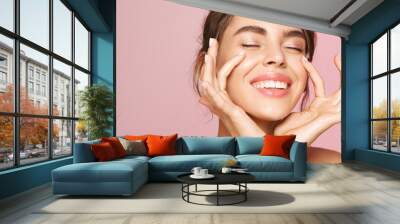 Skin care. Woman with beauty face touching healthy facial skin portrait. Beautiful smiling girl model with natural makeup touching glowing hydrated skin on pink background closeup Wall mural