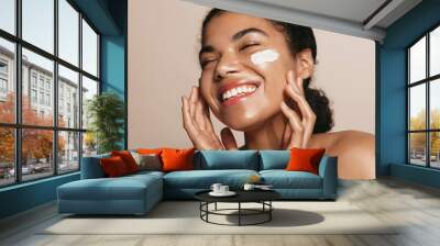 Smiling woman using skincare product. Female taking face cream to apply on facial skin Wall mural