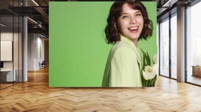 Stylish smiling girl with bouquet of flowers, laughing at camera, standing over green background Wall mural