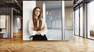 Successful young businesswoman lean wall and cross hands on chest, smiling confident and assertive, express readiness, just signed big financial deal for her company, standing inside office Wall mural