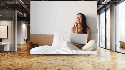 Work from home, freelance and lifestyle concept. Portrait of creative young asian female sitting on bed with laptop, smiling thoughtful and looking away while think-up. Girl shopping online Wall mural