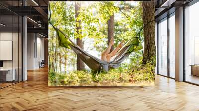 A green hammock hangs among the trees by the lake. A young girl is resting outdoors in a hammock. Picnic. Summer outdoor recreation with an overnight stay. Summer background Wall mural