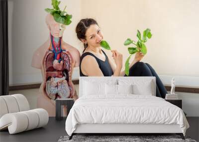 A yoga coach sits next to a medical dummy Wall mural