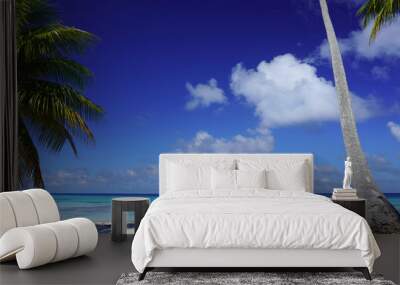 Two chairs on a sandy beach with palm trees and a turquoise lagoon under a bright blue sky with clouds on the island of Fakarava in French Polynesia Wall mural