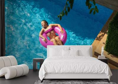 Happy beautiful girl relaxing in swimming pool with turquoise water. Girl floating on pink inflatable ring. Traveling and vacation concept. View from above Wall mural