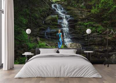 Girl traveler near a forest waterfall. Wall mural