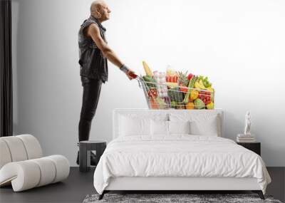 Bald man in leather clothes pushing a shopping cart full of food Wall mural