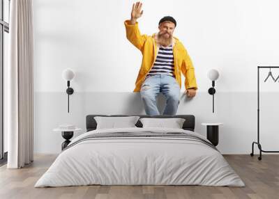 Bearded fisherman with a yellow rain coat sitting on a panel and waving Wall mural