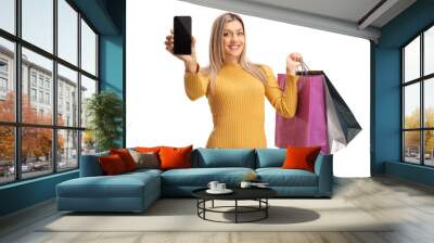 Blond woman showing a mobile phone and carrying shopping bags Wall mural