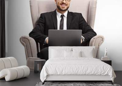 Businessman in an armchair with a laptop computer smiling at the camera Wall mural