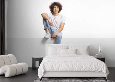 Casual young man with curly hair sitting on a blank panel Wall mural