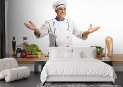 Cheerful mature male chef posing behing a kitchen counter with vegetables Wall mural