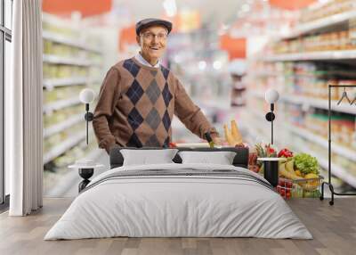 Elderly gentleman standing with a shopping cart full of food in a supermarket Wall mural