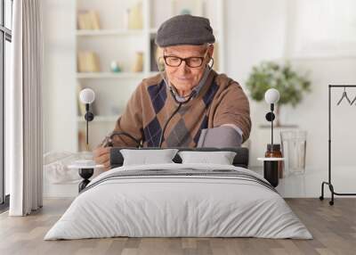 Elderly man checking blood pressure at home with pills in a bottle Wall mural