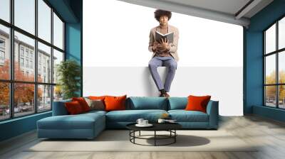 Elegant young man with curly hair sitting on a panel and reading a book Wall mural